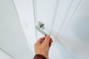 An individual gracefully opens a pristine white door by grasping its intricately designed handle
