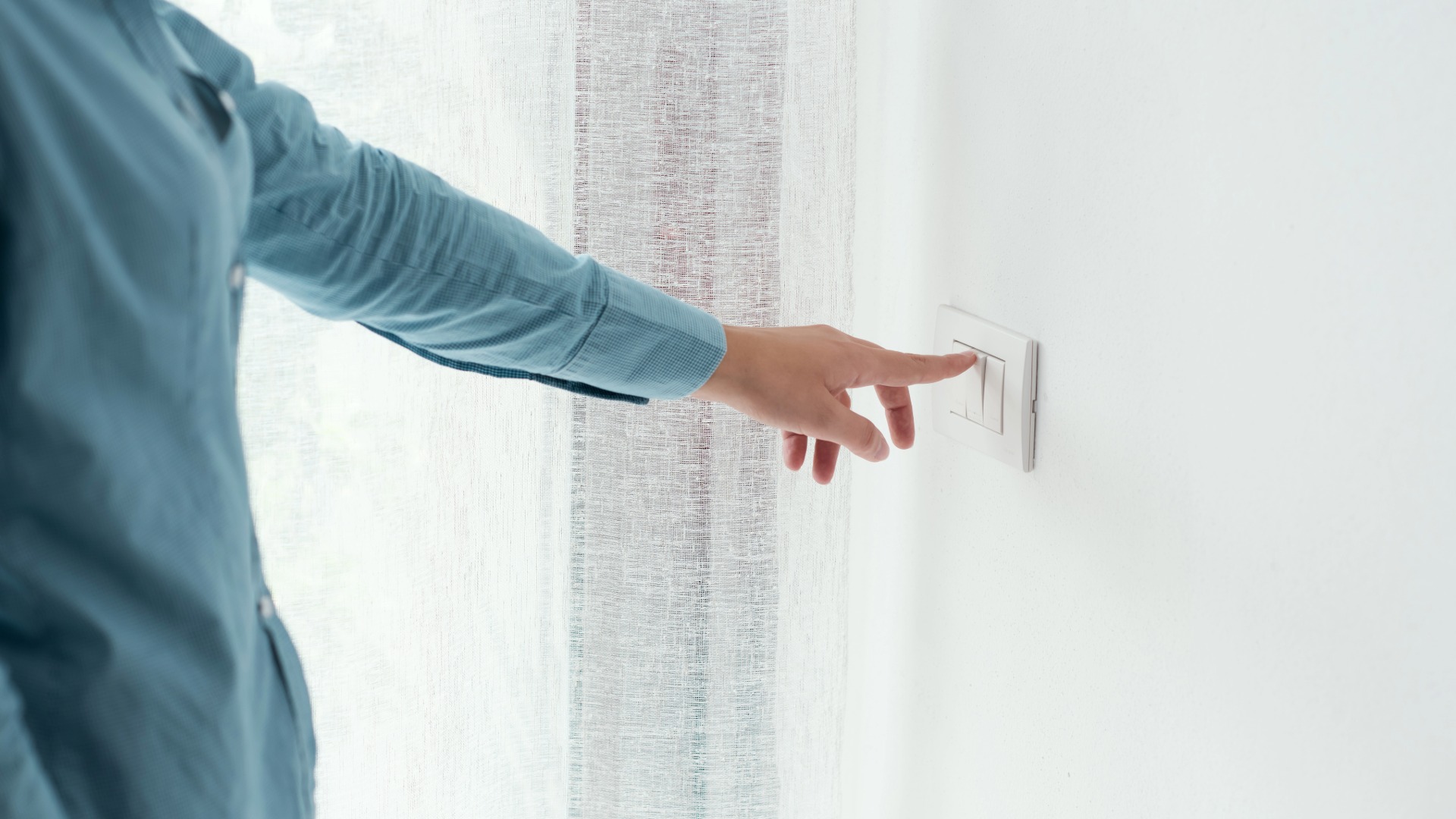 A person in a blue top pressing a light switch