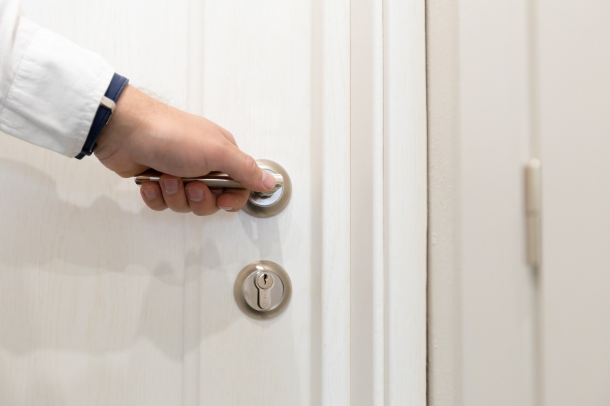 Hand reaching for door handle in a modern home environment during daylight hours